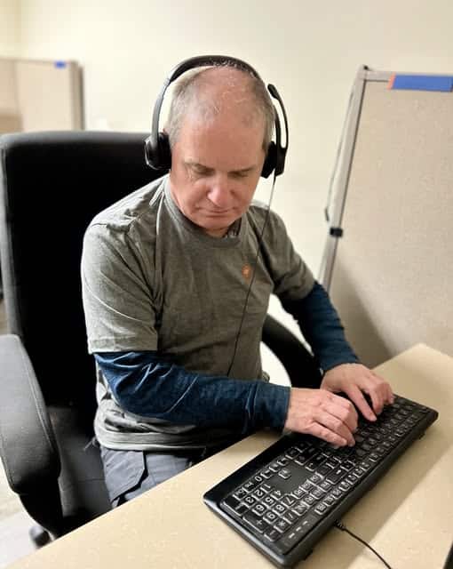 Randy is working in the call center typing on a keyboard while listening to the person on the other end of the line. 