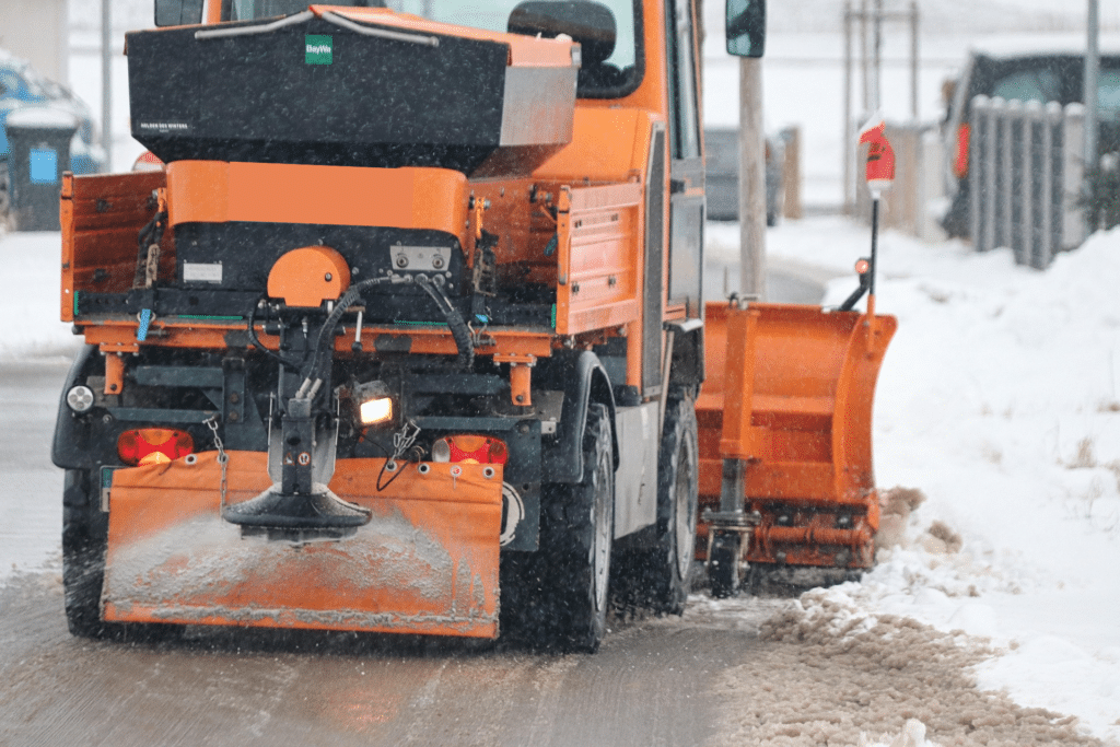 A snow plow is removing snow and spreading snow melt to the road. 